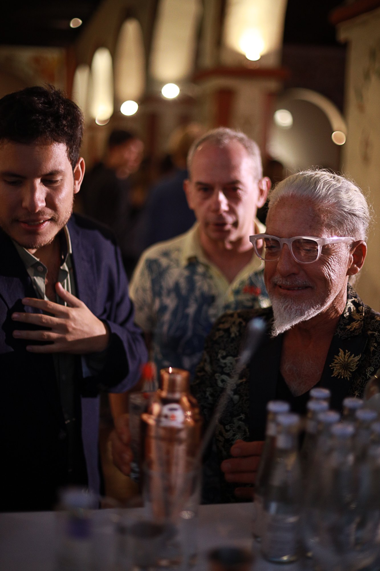 Guests raising cocktails in a toast at a private gathering, warm low light